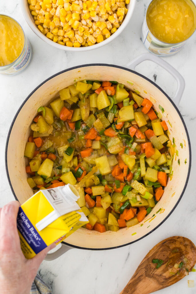 Pouring chicken broth into the cooked vegetables to make the base of the soup.