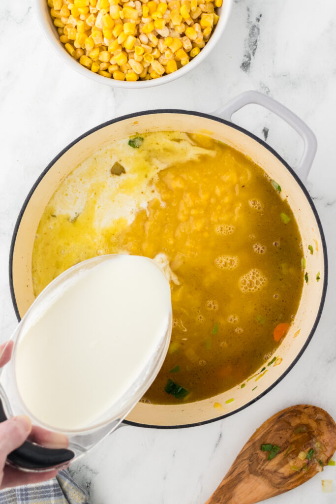 Pouring whole milk into the chicken broth to create a creamy base for the corn chowder.