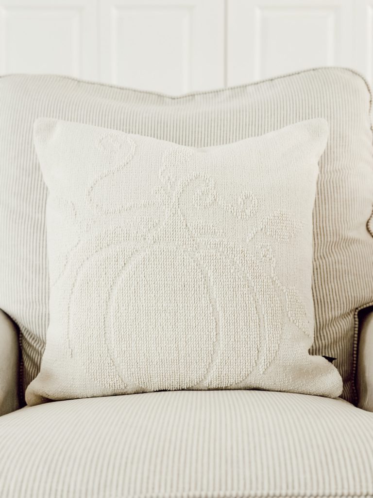 Pumpkin throw pillow on striped arm chair in living room for autumn.