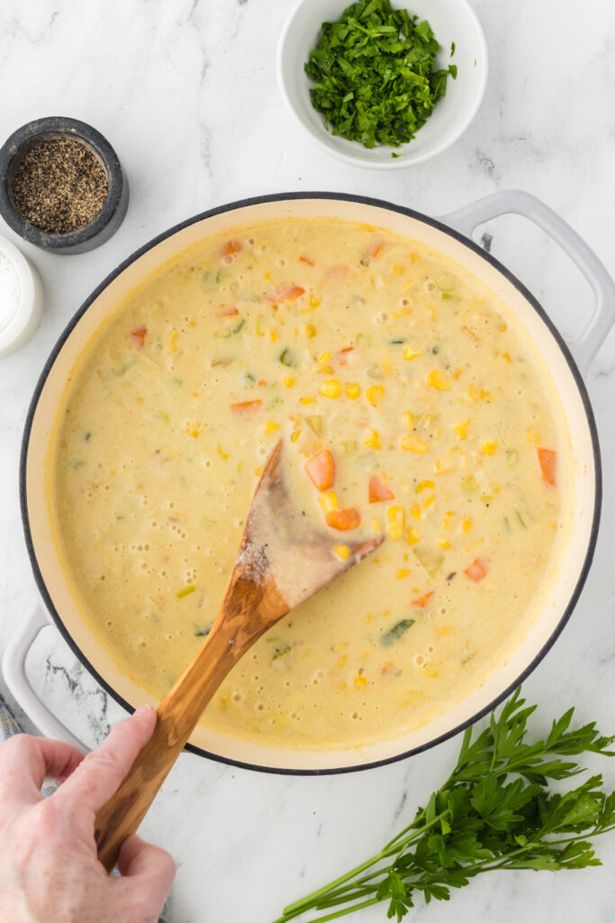 Stirring the corn into the chowder base to create a creamy corn chowder dish.