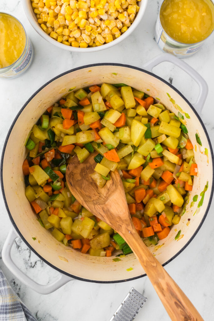 Stirring the sauted vegetables in the soup pan with a wooden spoon so they cook evenly.