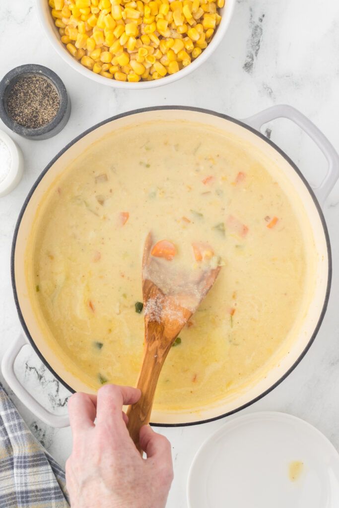 Stirring the slurry into the corn chowder with a wooden spoon to combine ingredients.