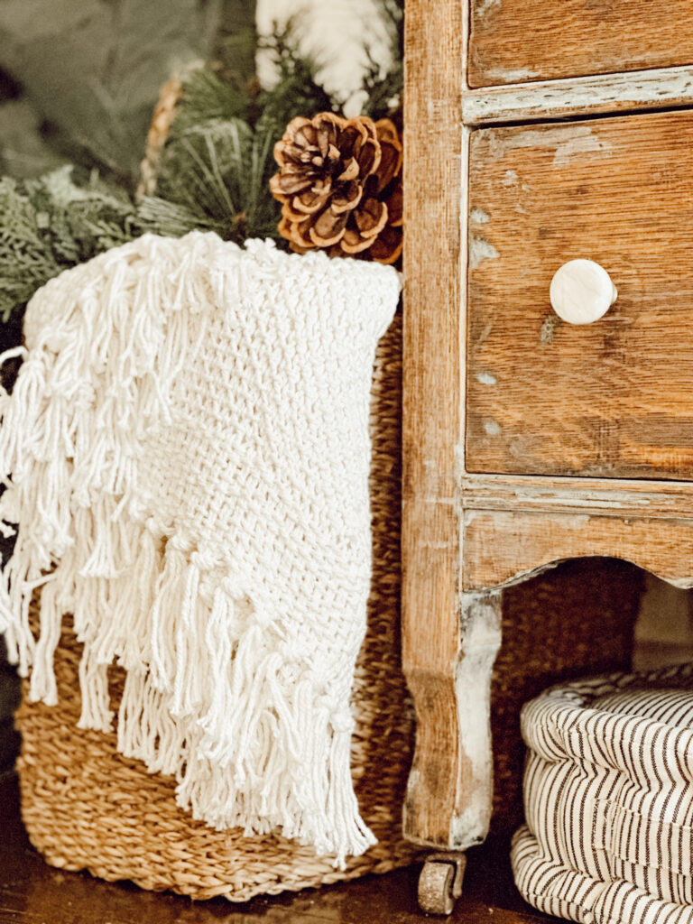 Easily transition your fall decor to Christmas decorations with a throw blanket in a basket with greenery and pine cones.