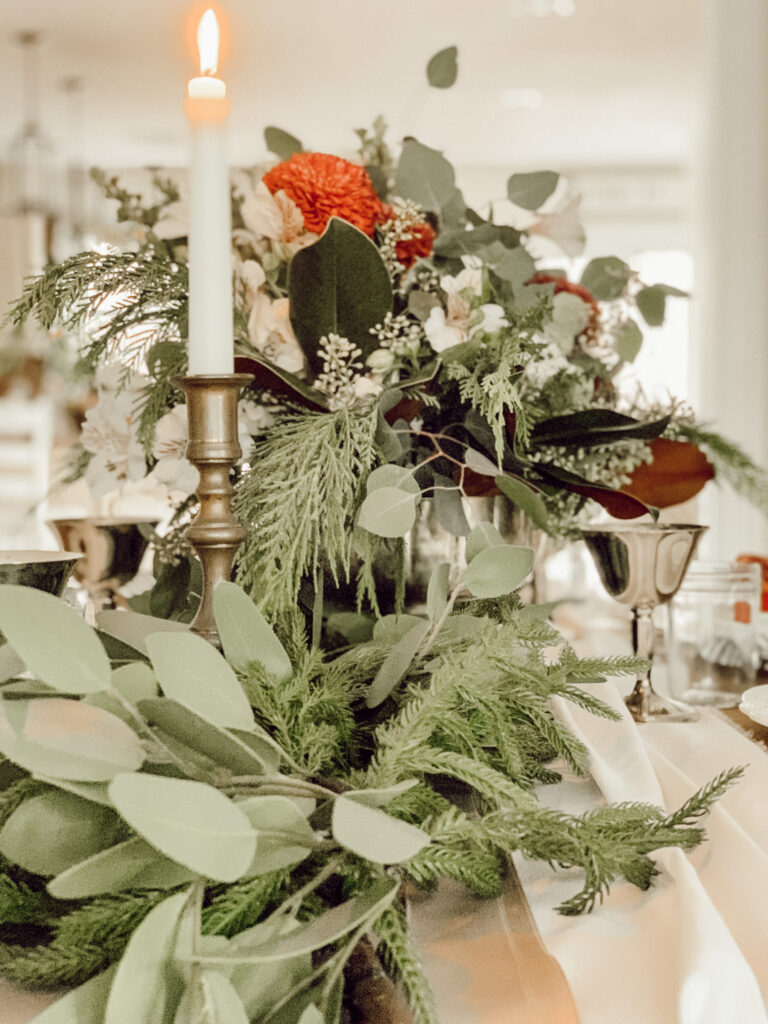 Fall to Christmas tablescape with a candle, eucalyptus, and evergreens on a tablescape.