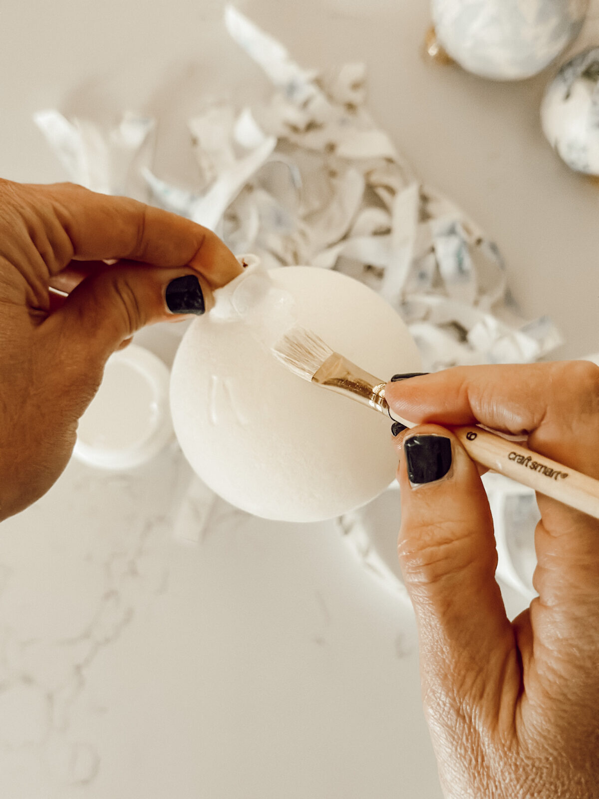 Using a paintbrush, brush Mod Podge onto the Christmas ornament before adding fabric strips.