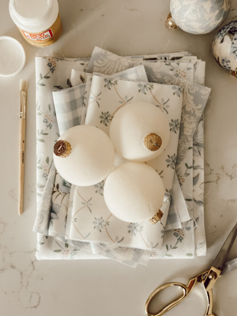 Fabric, round glass ornaments, scissors, Mod Podge, and a paintbrush are the supplies you'll need to make your own DIY decoupage ornaments.