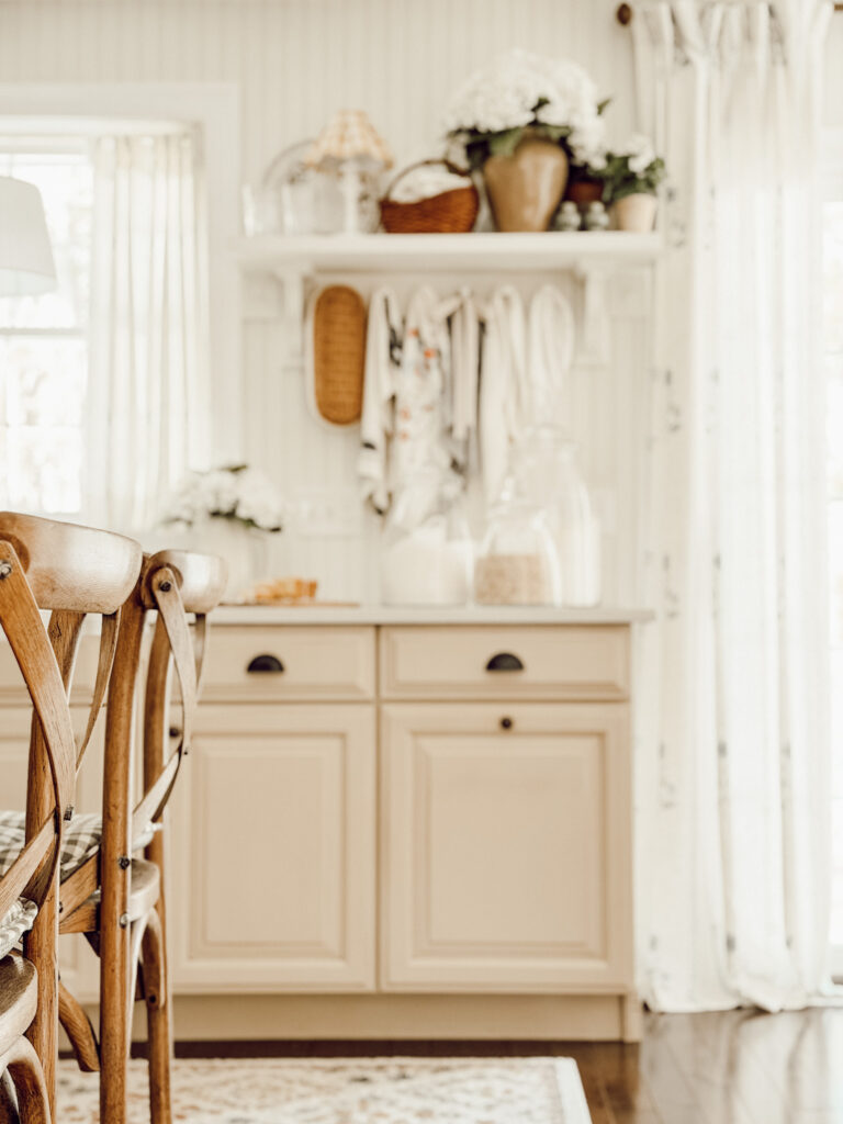 Cozy cottage kitchen with cozy home accents like wooden chairs, woven baskets, and flowers.