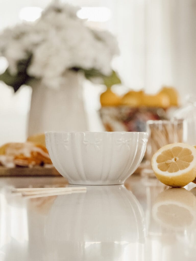 A cozy vignette on the kitchen counter includes a candle, loaf of lemon bread, a bowl of lemons, and a vase of flowers.