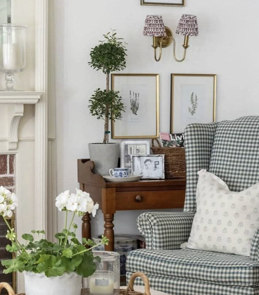 Gingham accent chair in cozy cottage living room with a topiary, sconces, and a potted geranium.