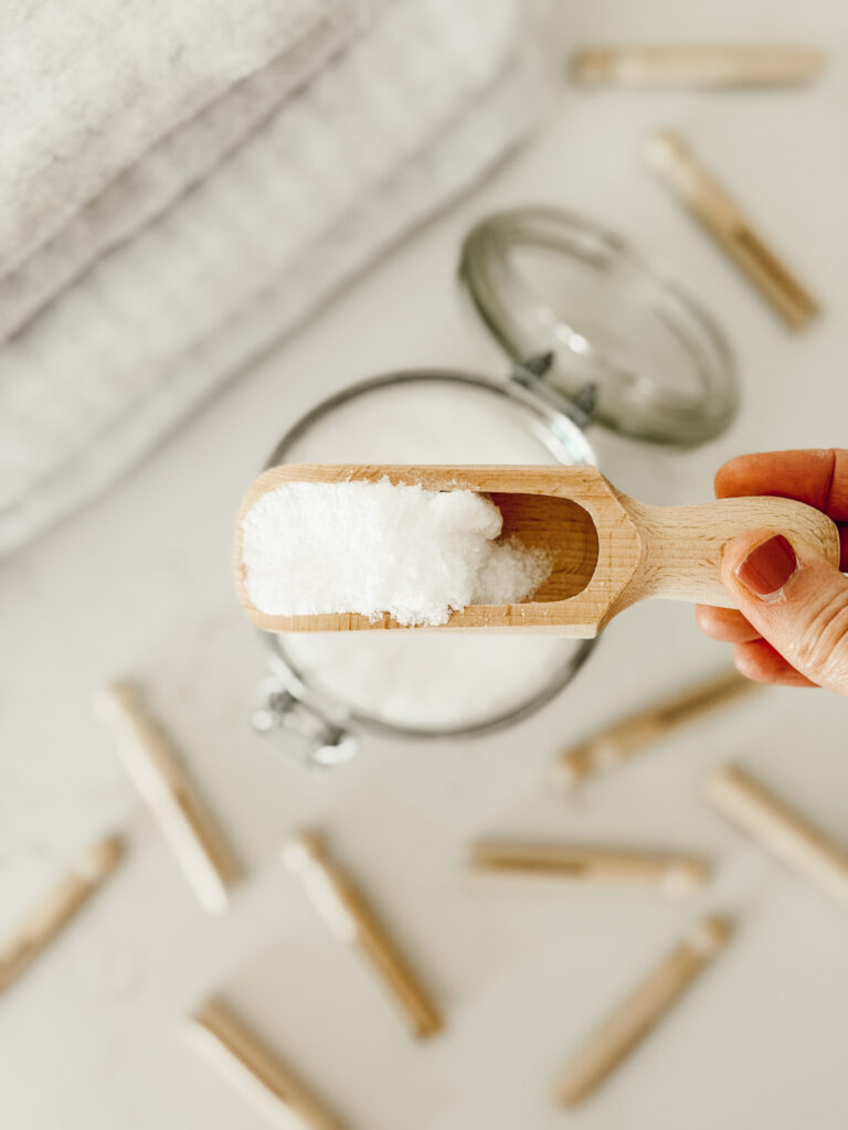 Scoop of DIY natural laundry scent booster in a glass jar with a wooden scoop.