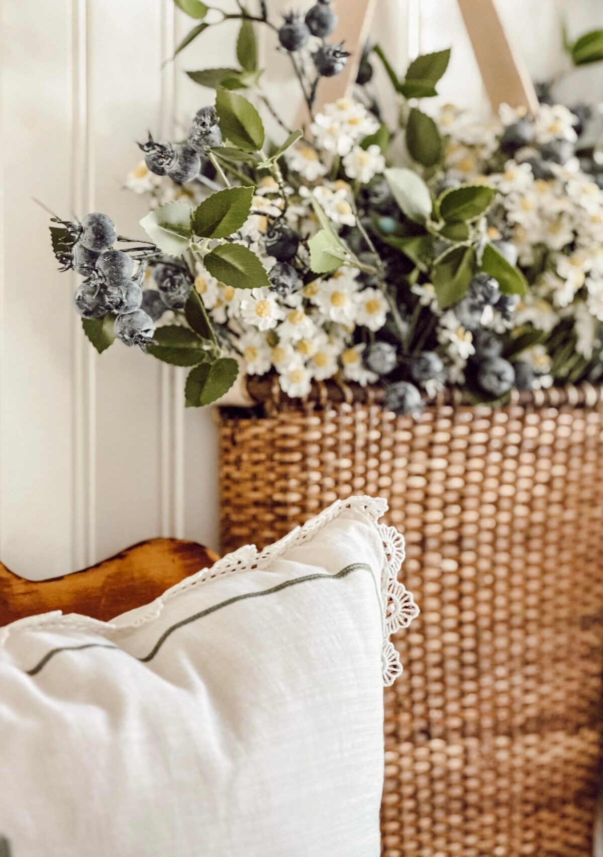 Basket of ground apple flowers and blueberry stems hanging on the wall in a cottage style home.