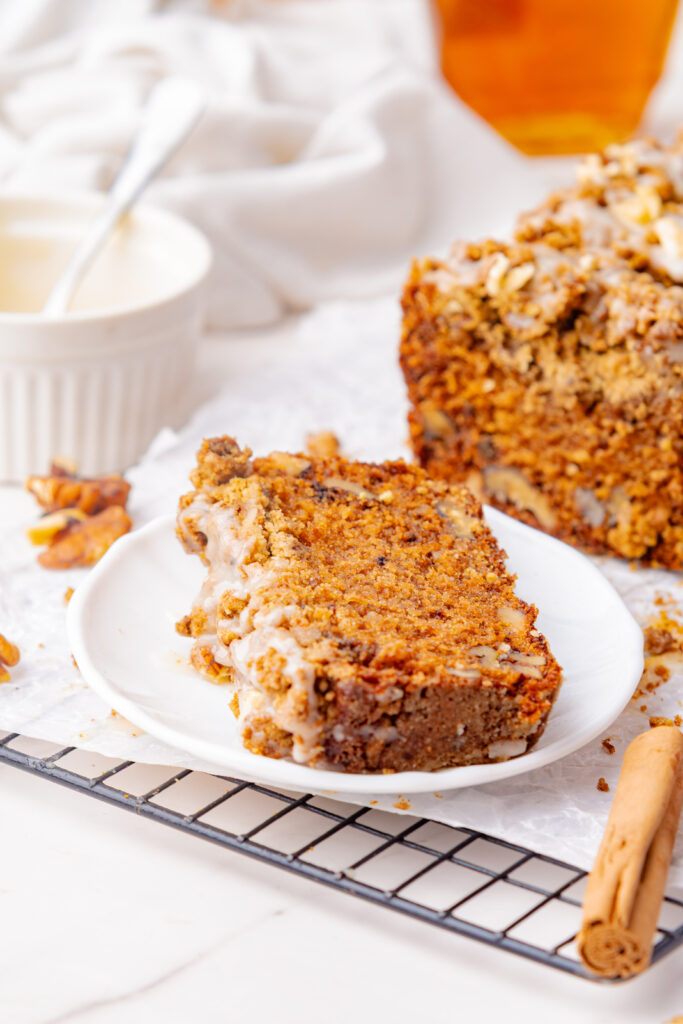 A small white dessert plate with a slice of coffee cake drizzled with maple glaze.