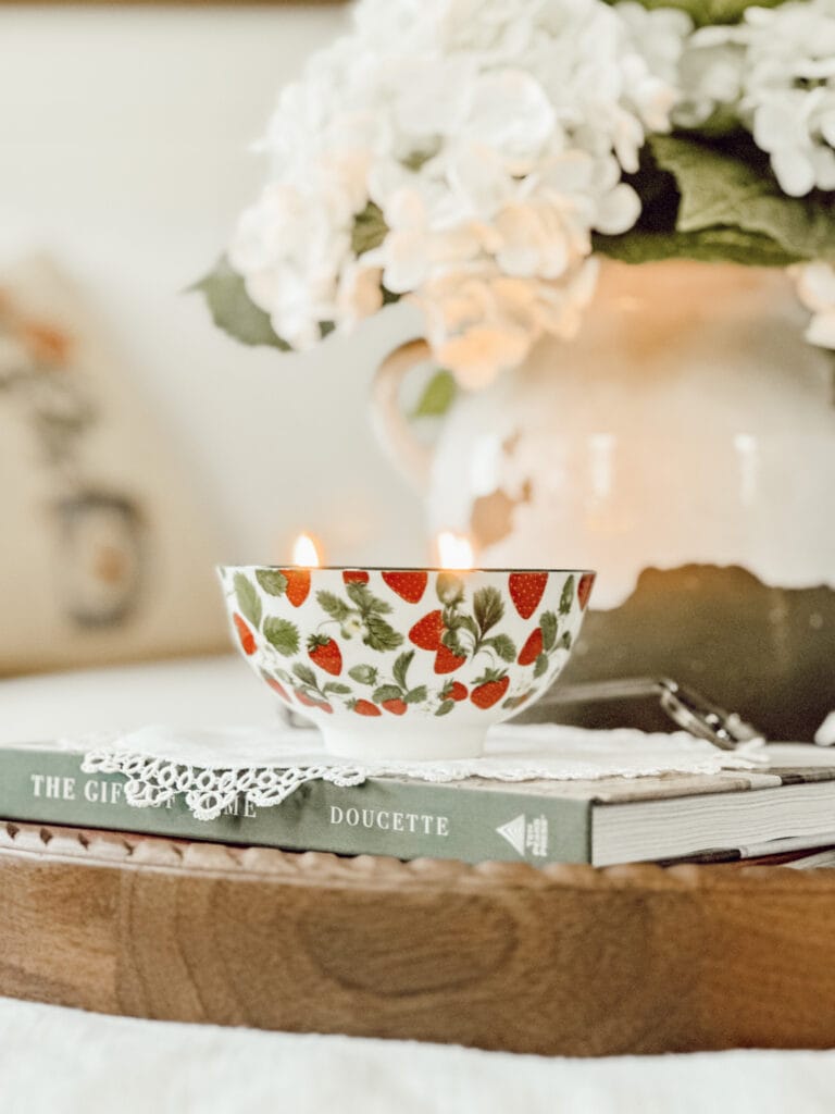 Seasonal summer candle burning on a round wooden tray on an ottoman in the living room.
