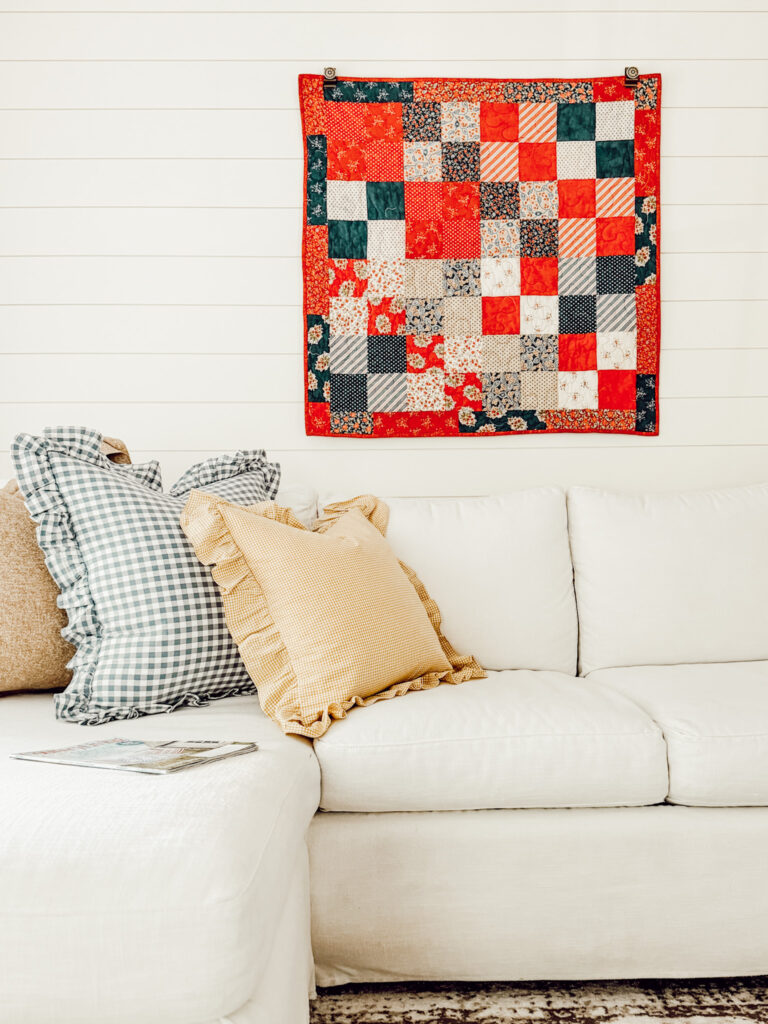 Vintage quilt hanging on living room wall behind white couch with throw pillows.