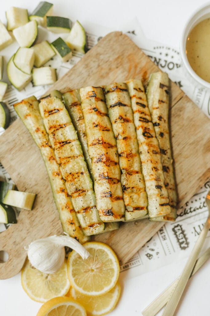 Marinated grilled zucchini spears on a wooden cutting board for serving a summer side dish.