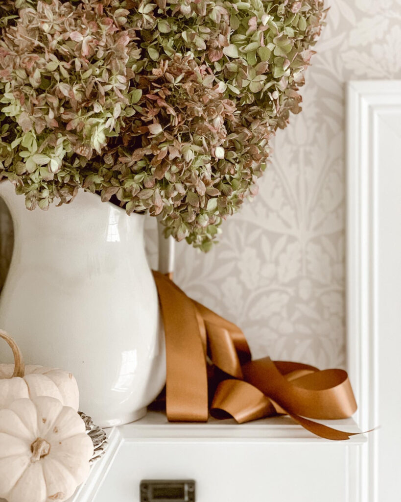 Dried hydrangeas in a vintage ironstone pitcher with a copper colored ribbon tied in a bow.