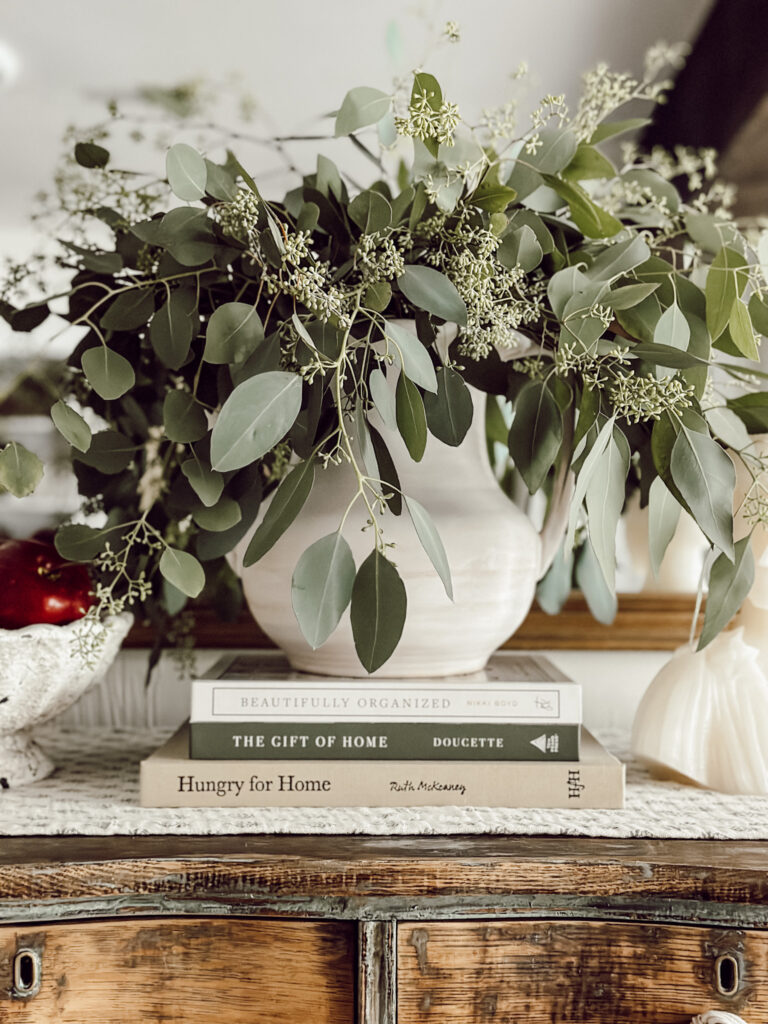 Easy fall flower arrangement ideas for cozy autumn decor include this cream vase with seeded eucalyptus stems.