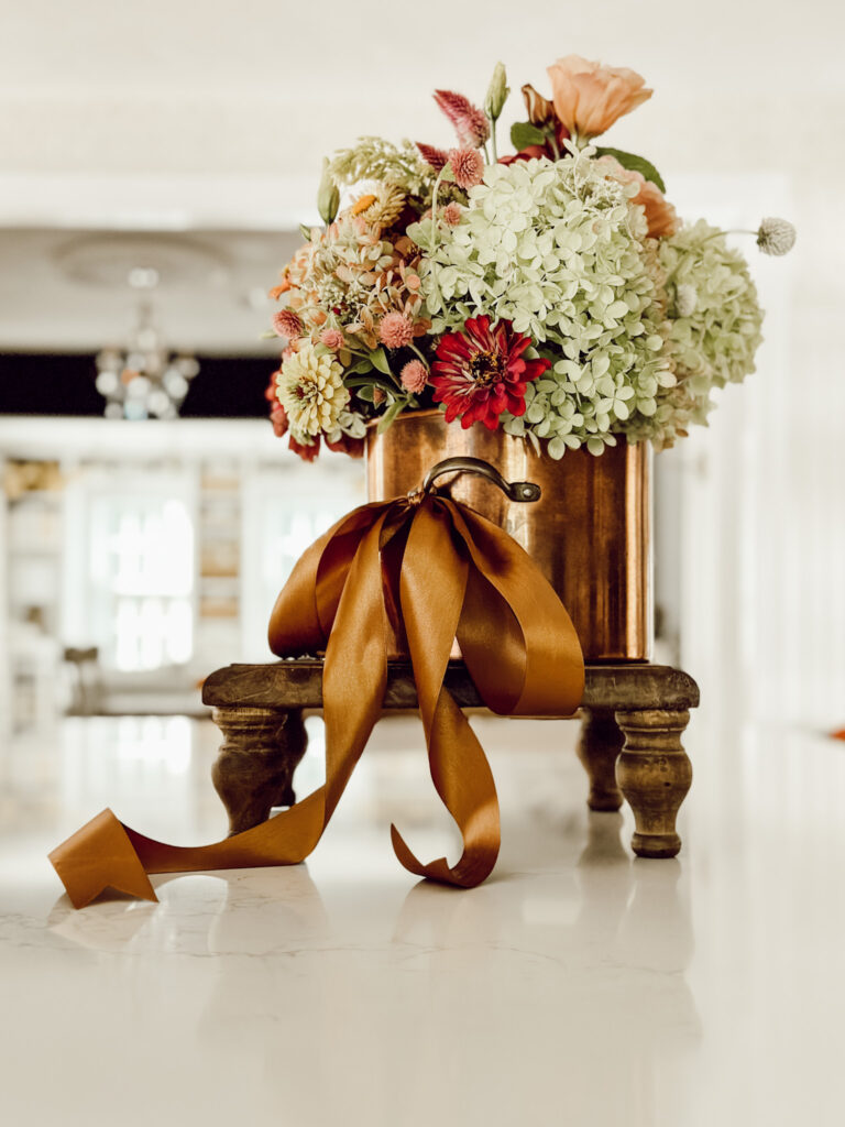 Fresh fall flowers in an old copper pot on a wooden riser on kitchen countertop.