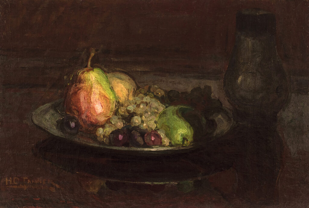 Pears and other fruit in a bowl with a glass on a wooden table.