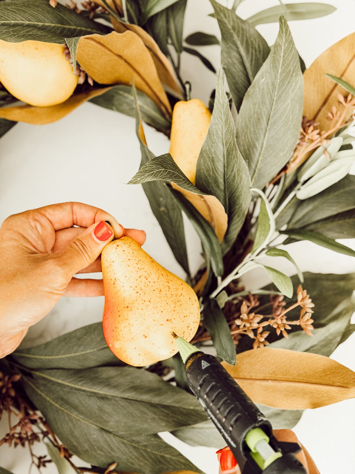 Using a hot glue gun to attach faux pears to a fall wreath for autumn.