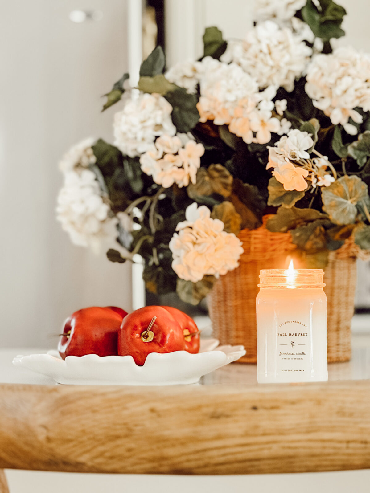Kitchen countertop styled for fall with a bowl of red apples, pumpkin candle, and faux fall flowers.