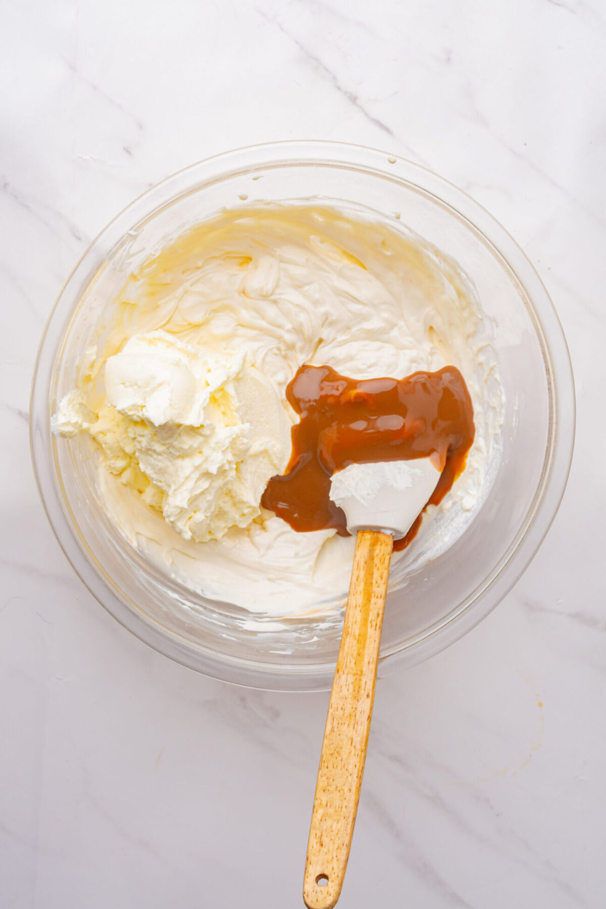 Caramel sauce added to the cream cheese dip mixed together with a rubber spatula in a large mixing bowl.
