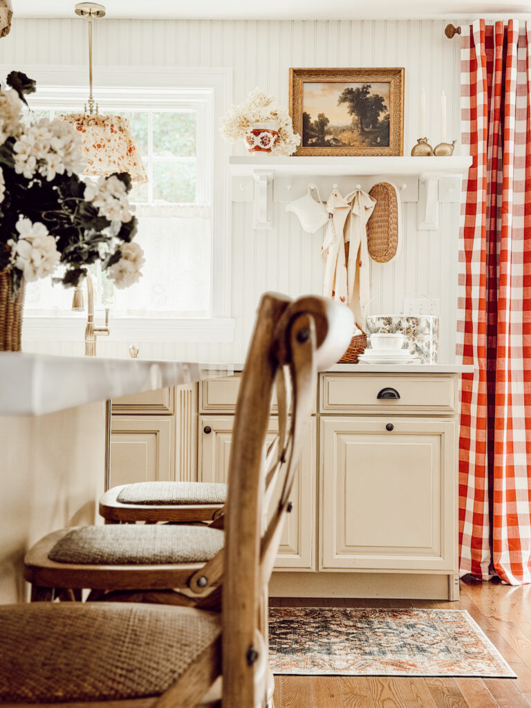 Country cottage kitchen with fall decorations, wooden chairs, and red buffalo check curtains.