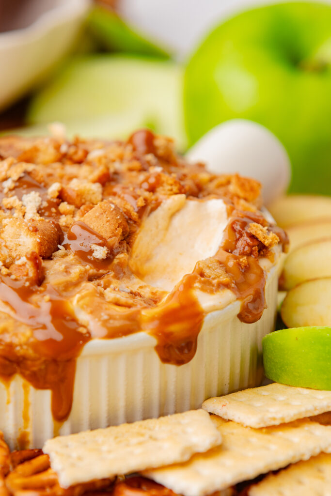 Dulce de leche apple dip on a wooden board with apple slices, crackers, and pretzels.
