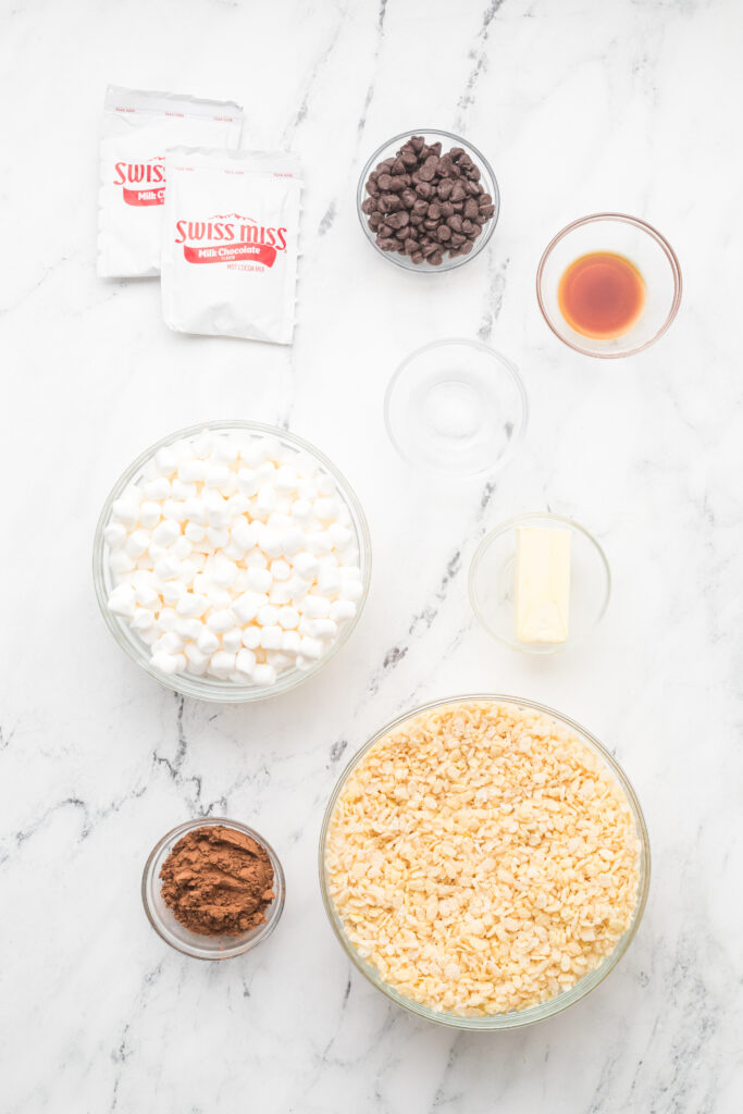 Simple ingredients to make cocoa Rice Krispie treats include mini marshmallows, rice cereal, butter, vanilla extract, hot cocoa mix, and chocolate chips.