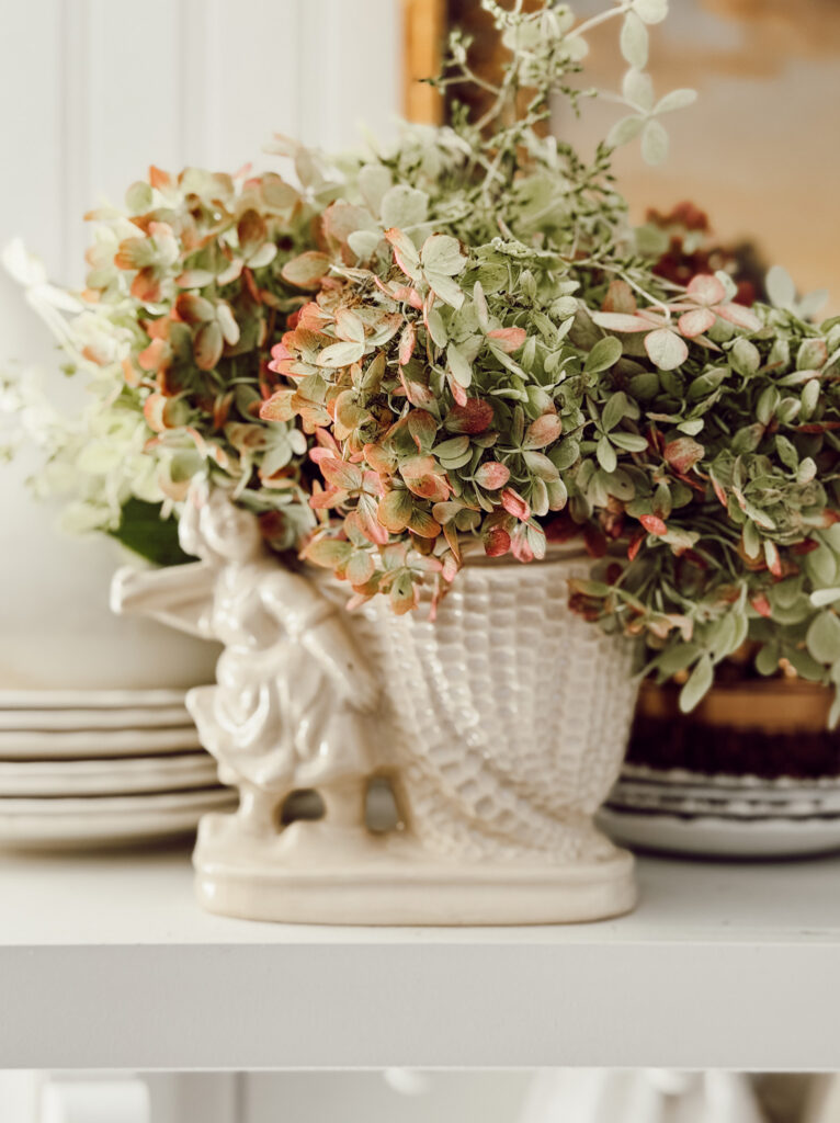 Fall decorating with hydrangea blooms for cozy home decor. Hydrangea stems tucked into a vintage vessel on a kitchen shelf.