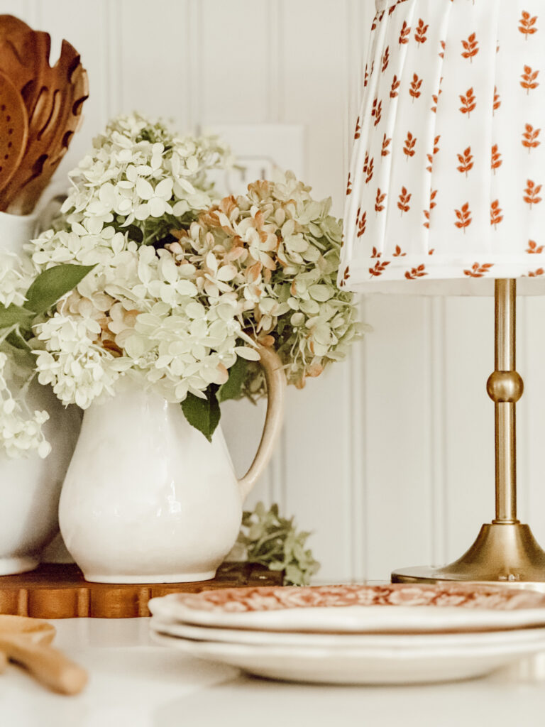 Vintage ironstone pitcher filled with hydrangea blooms with vintage plates and a small lamp.